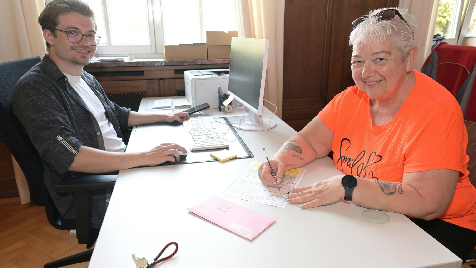 Der Mitarbeiter der Stadt sitzt am Computer. Die Wählerin füllt ein Formular aus.