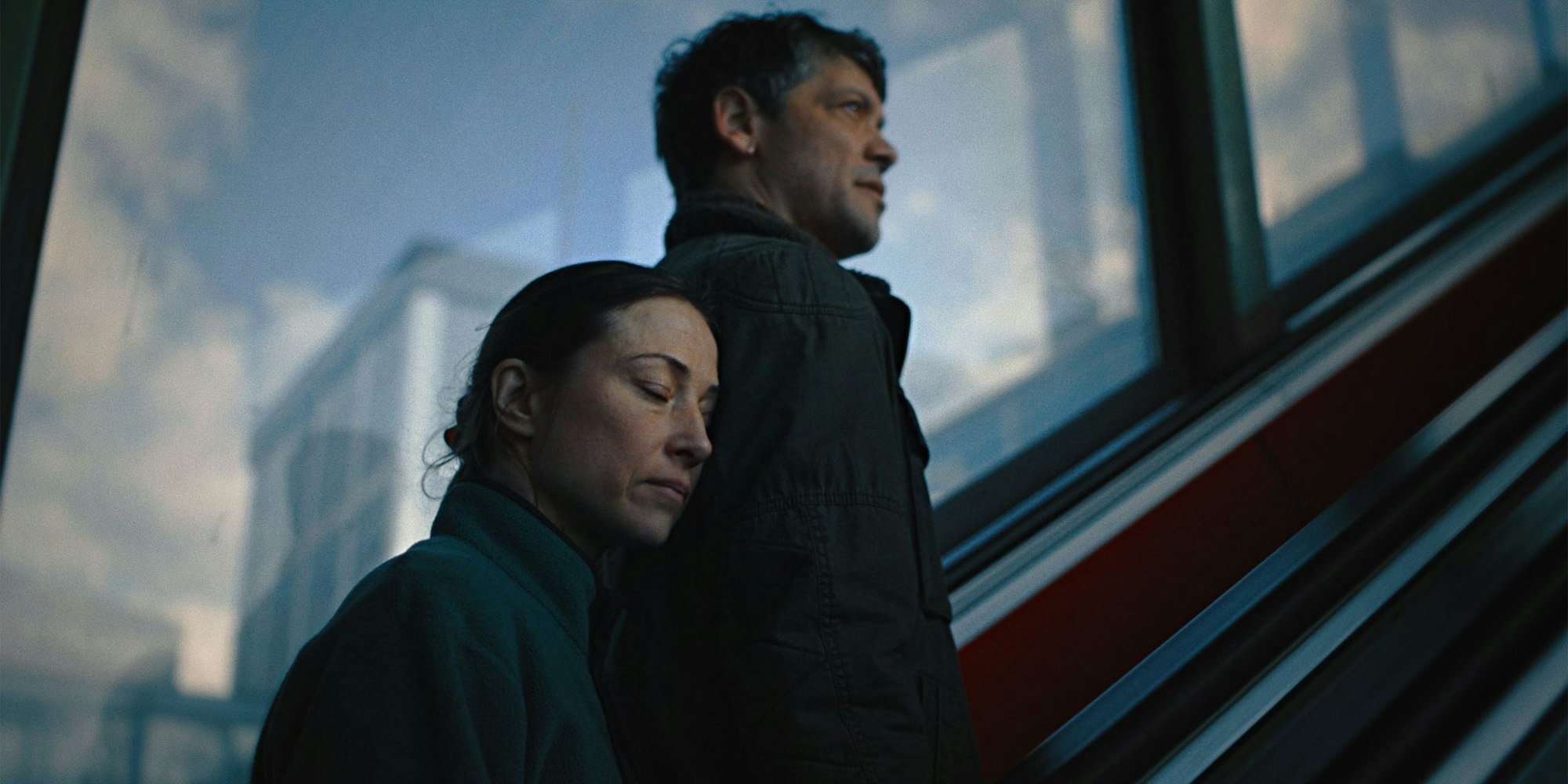 Eine Frau schmiegt sich auf einer Rolltreppe nah an einen Mann