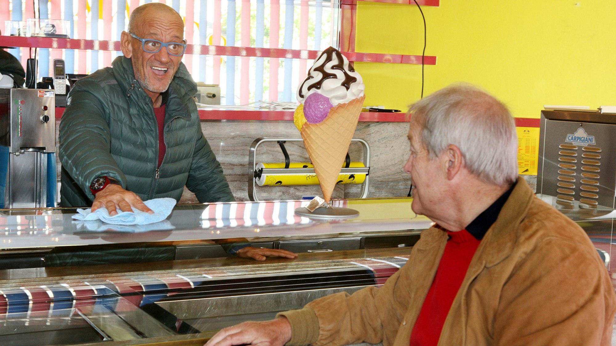 Henoch Mares steht hinter der Theke seines italienischen Eiscafés Mares in Heidkamp und wischt das Thekenglas. Dabei schaut er durch seine hellblaue Brille in die Augen eines Gastes, der es sich an der Theke gemütlich gemacht hat.
