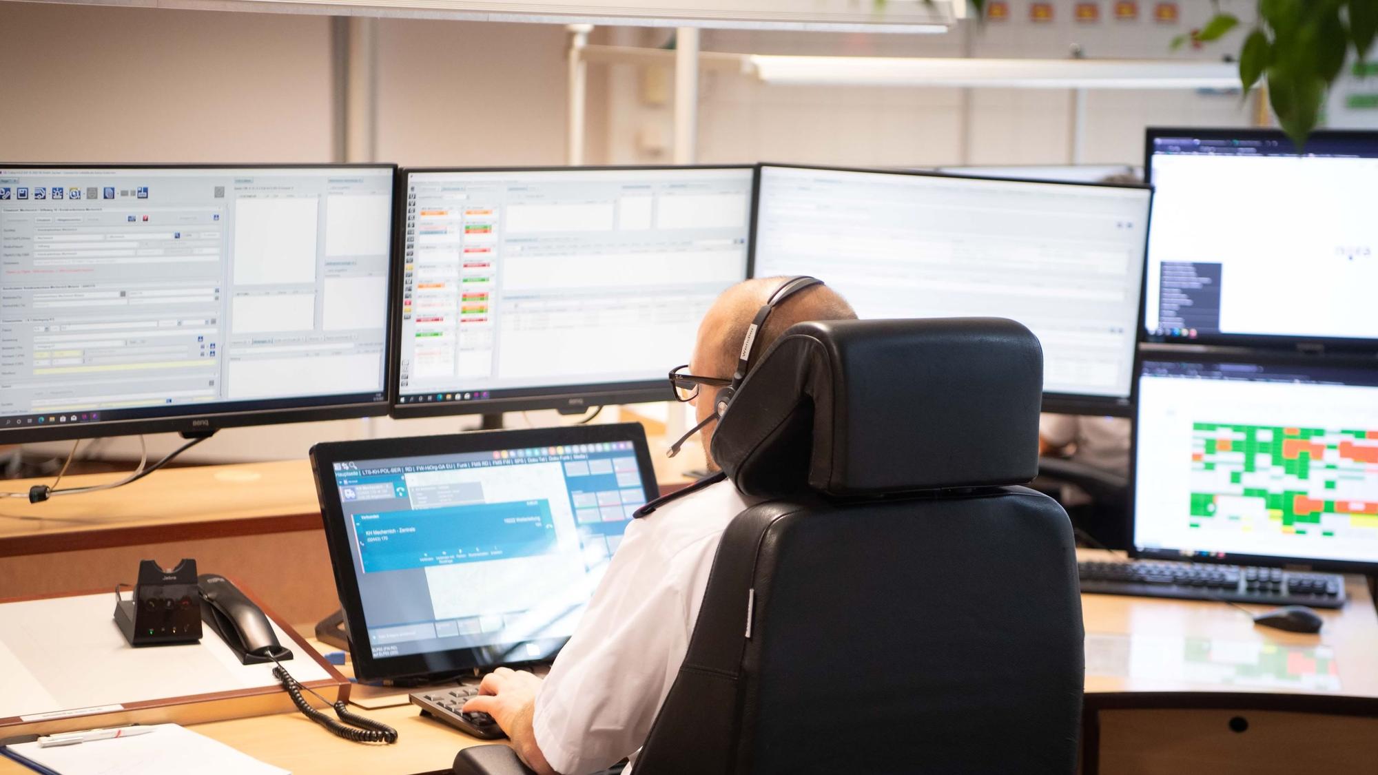 Das Bild zeigt einen Disponenten in der Leitstelle, der vor zahlreichen Monitoren sitzt.