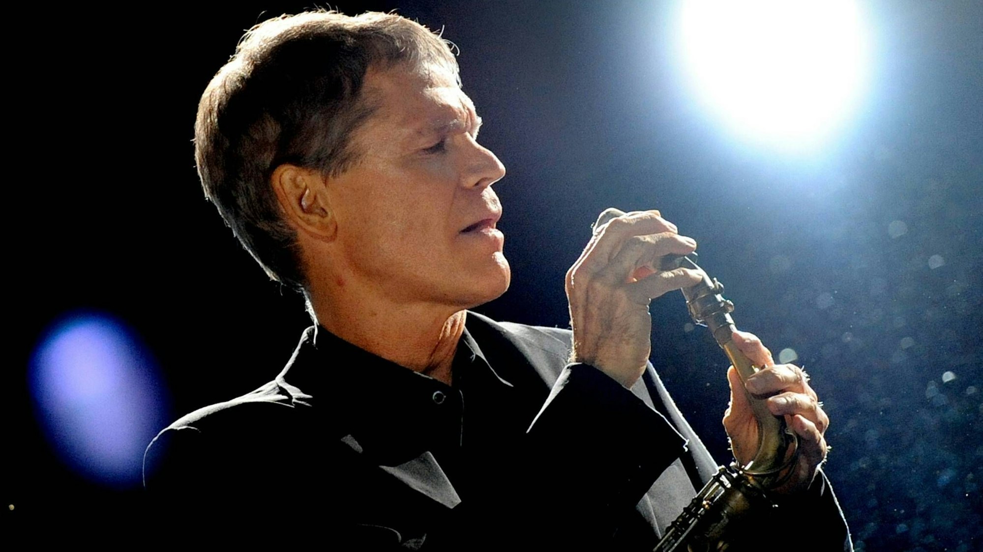 David Sanborn trägt einen schwarzen Anzug und justiert das Mundstück seines Altsaxofons.