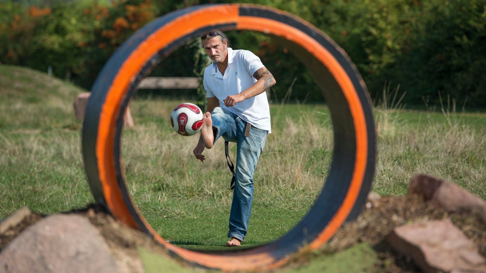 Ein Mann schießt einen Ball barfuß durch ein rundes Hindernis.
