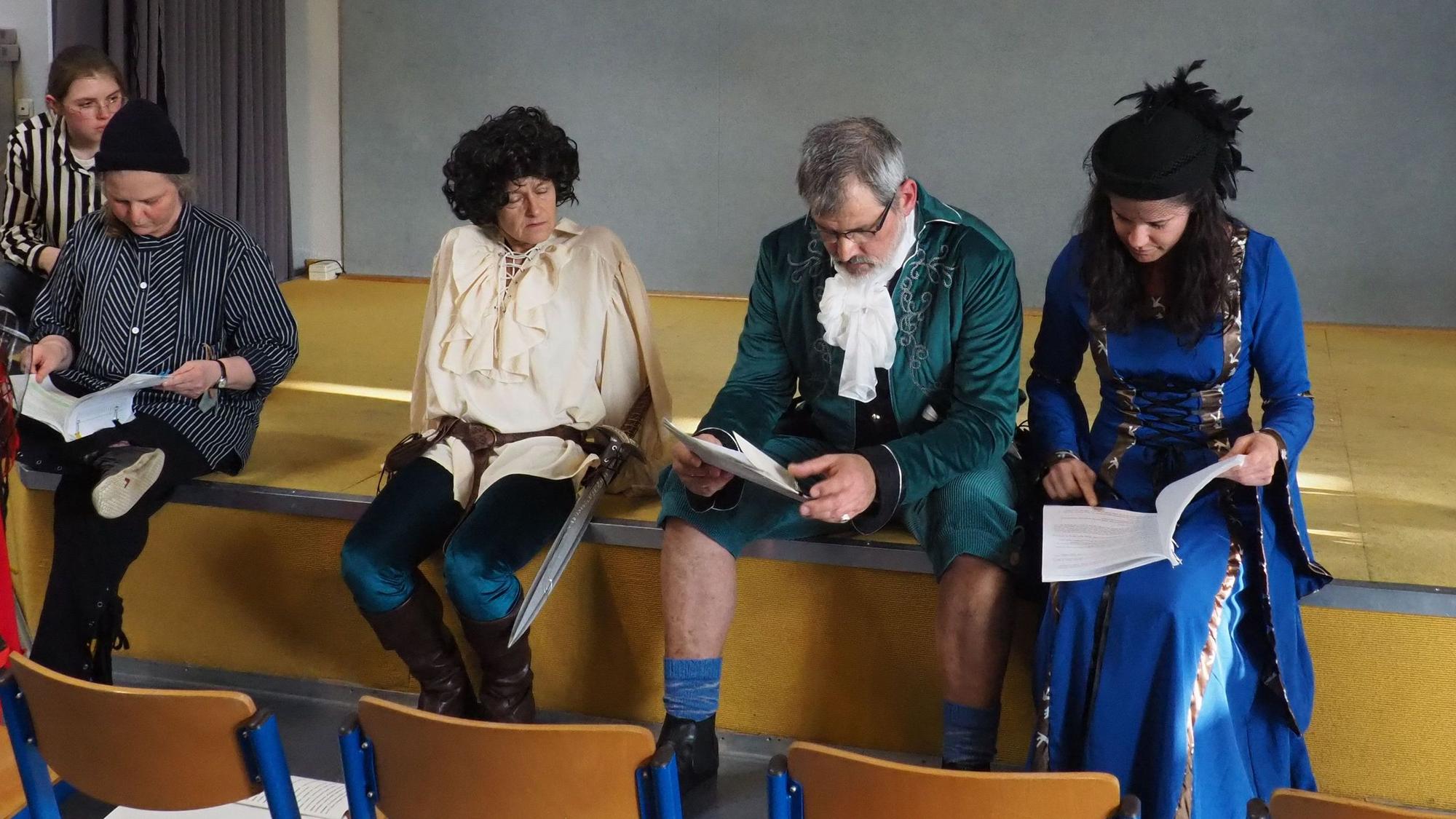 Die Schauspieler sitzen auf dem Rand der Bühne und studieren ihre Texthefte.