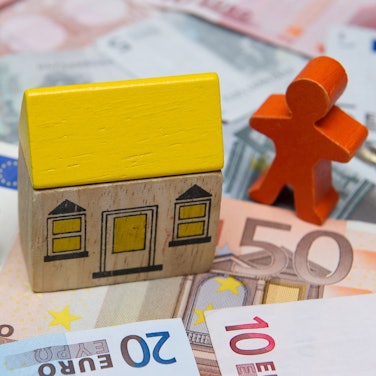 Ein kleines Spielzeughaus steht auf Euro-Geldscheinen.