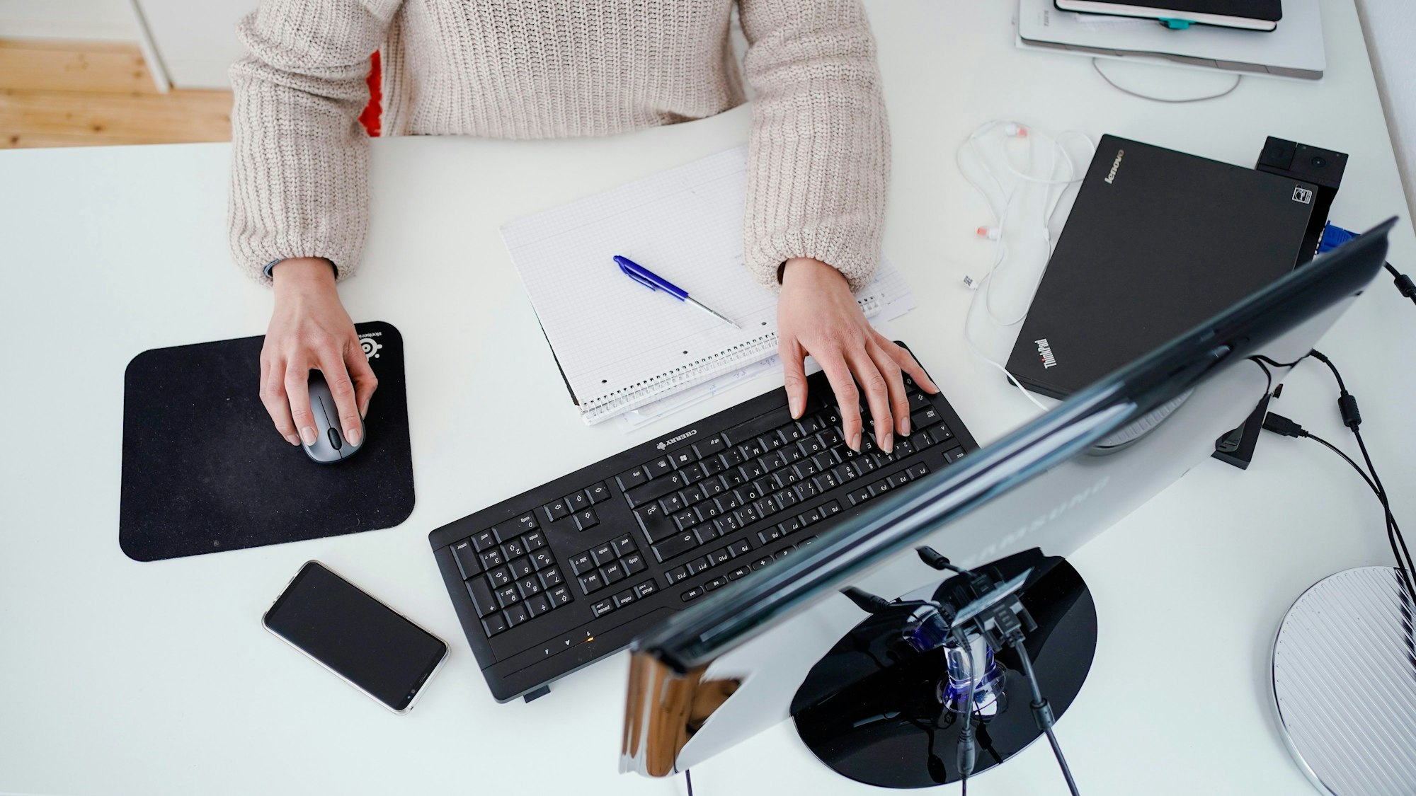 Blick von oben auf einen Schreibstisch, an dem eine Person an einem Computer arbeitet.