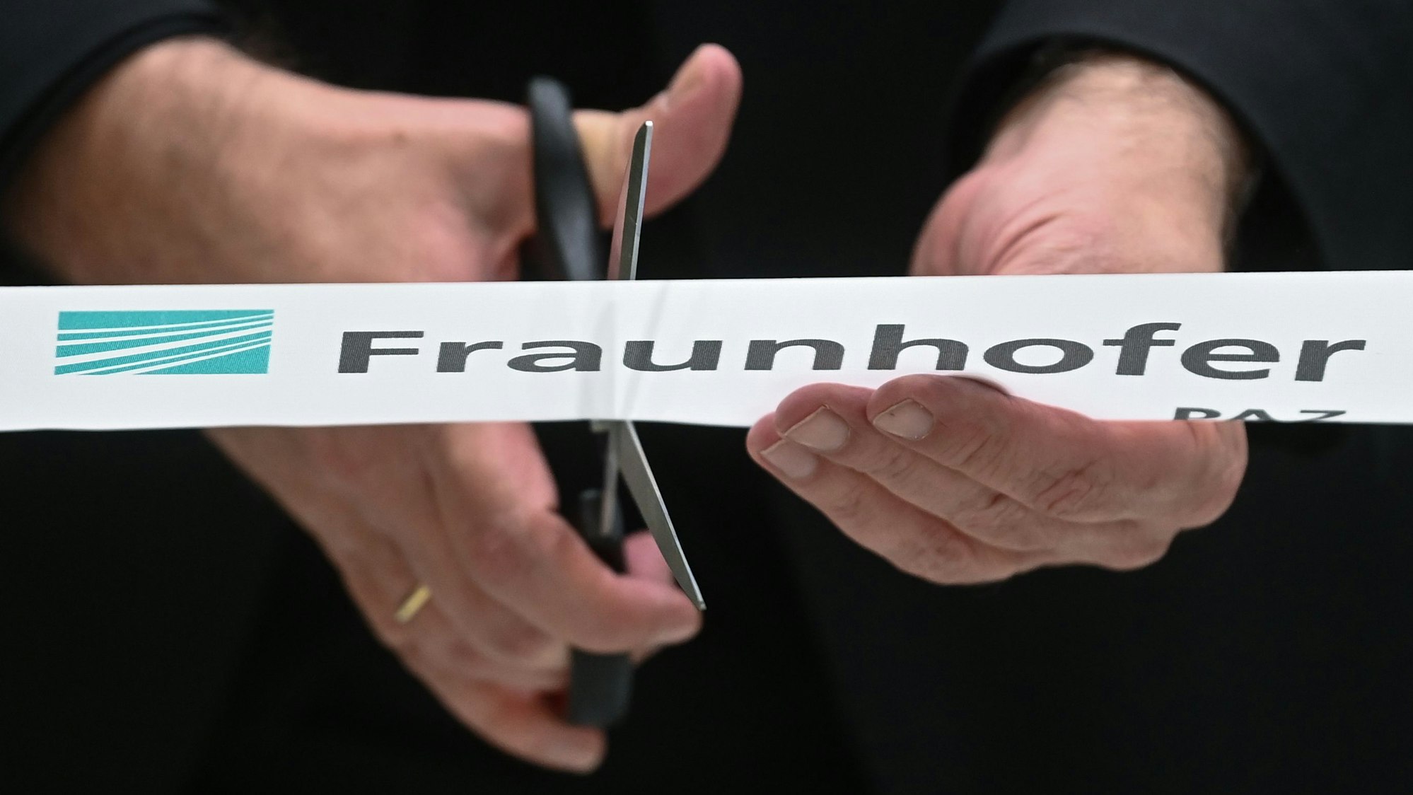 Auf dem Bild sind zwei Hände mit einer Schere zu sehen: Ein Band mit der Aufschrift „Fraunhofer“ wird durchschnitten.