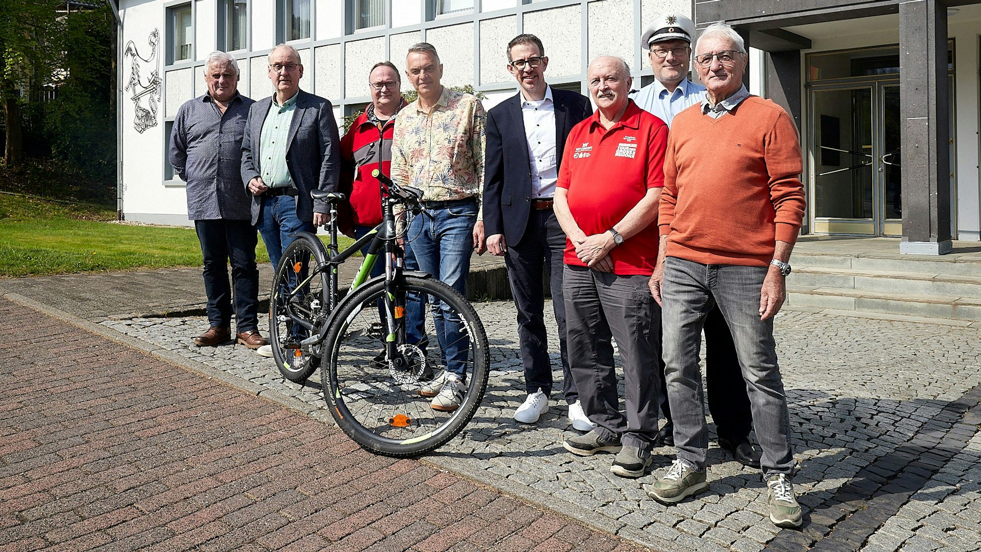 Acht Männer stehen vor dem Rathaus in Hellenthal an einem Fahrrad.