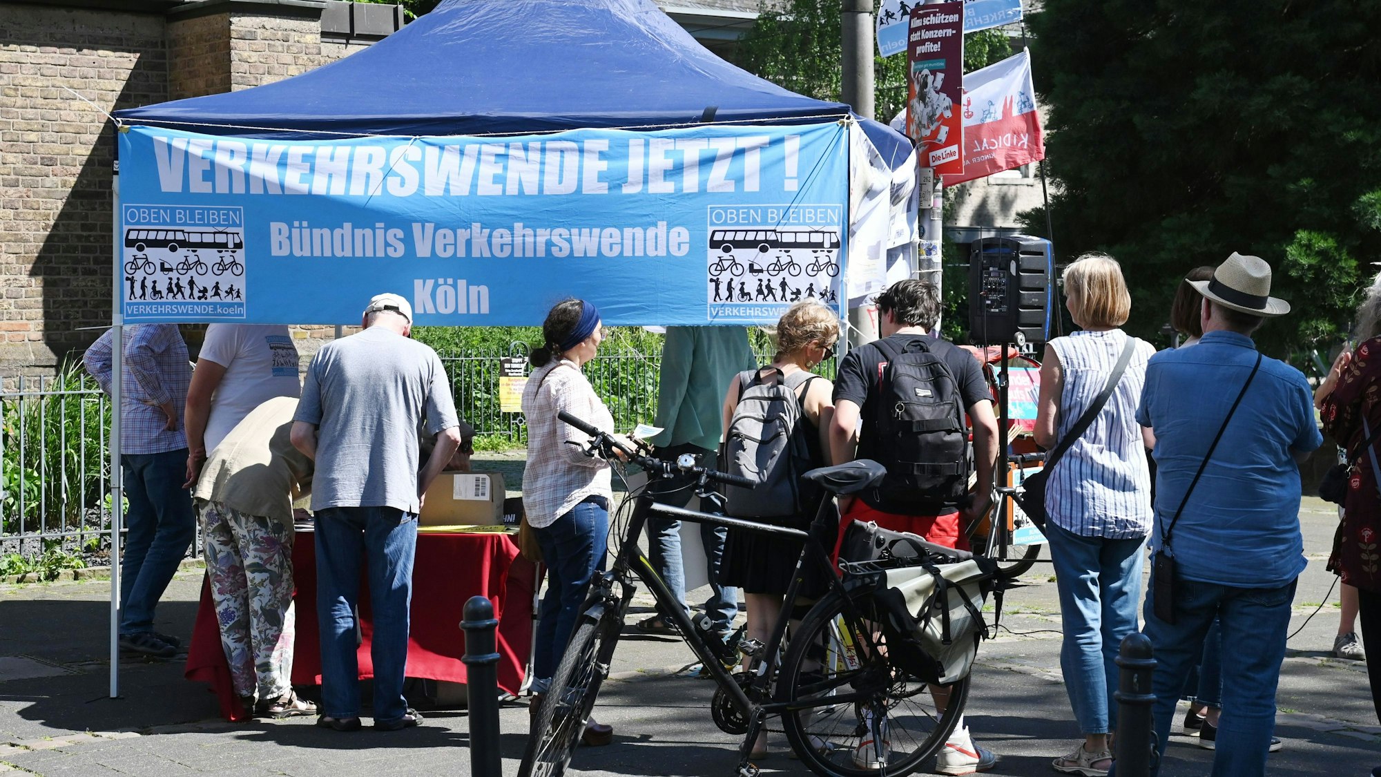 Menschen stehen an einem Pavillon, auf einem Transparent steht „Verkehrswende jetzt“.