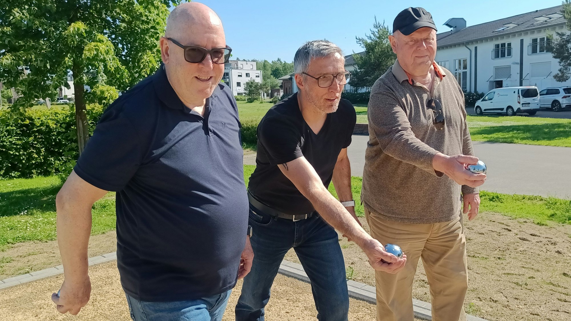 Drei Männern setzen zum Wurf ihrer Boule-Kugeln an.