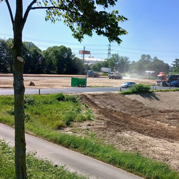 Erdarbeiten mit schweren Fahrzeugen auf zwei durch eine Straße getrennten Grundstücken.