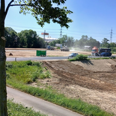 Erdarbeiten mit schweren Fahrzeugen auf zwei durch eine Straße getrennten Grundstücken.