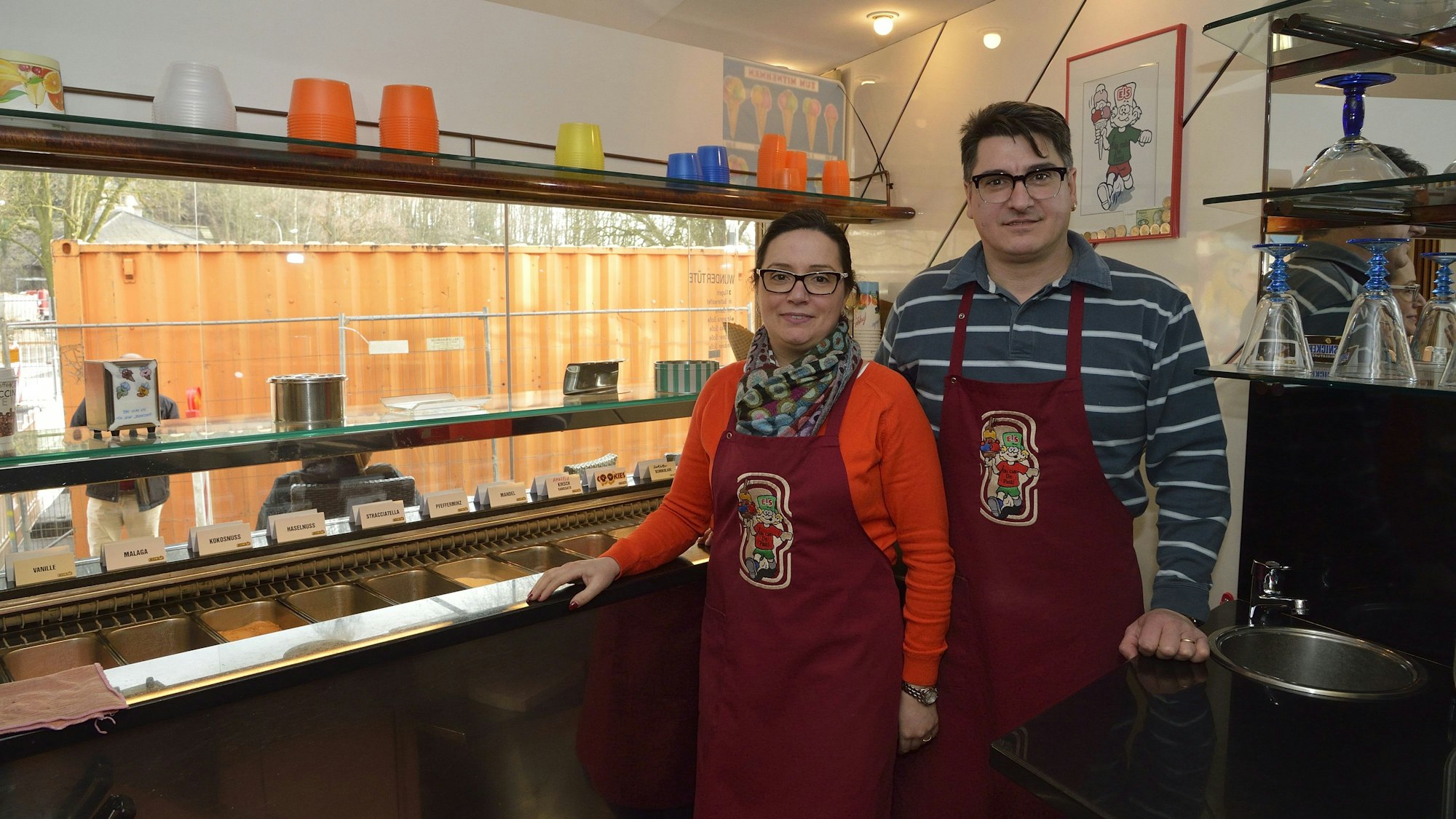 Sonia Stefani (l.) und ihr Ehemann Simone (r.) in den Räumlichkeiten ihres Eiscafés im Jahr 2017. Sie stehen vor einer Eistheke und lächeln in Richtung der Kamera.