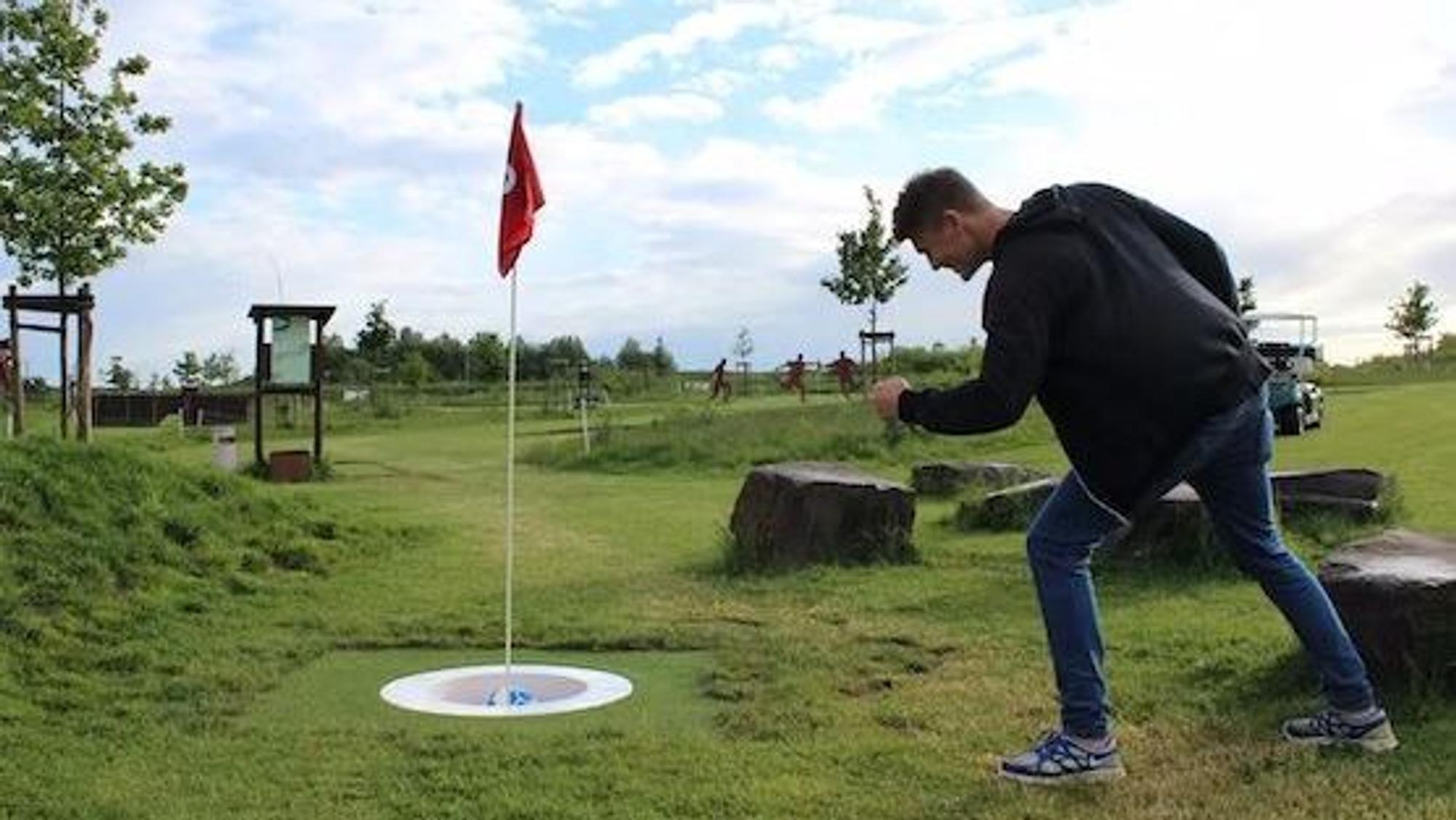 Ein Mann freut sich über einen im Loch versenkten Fußball.