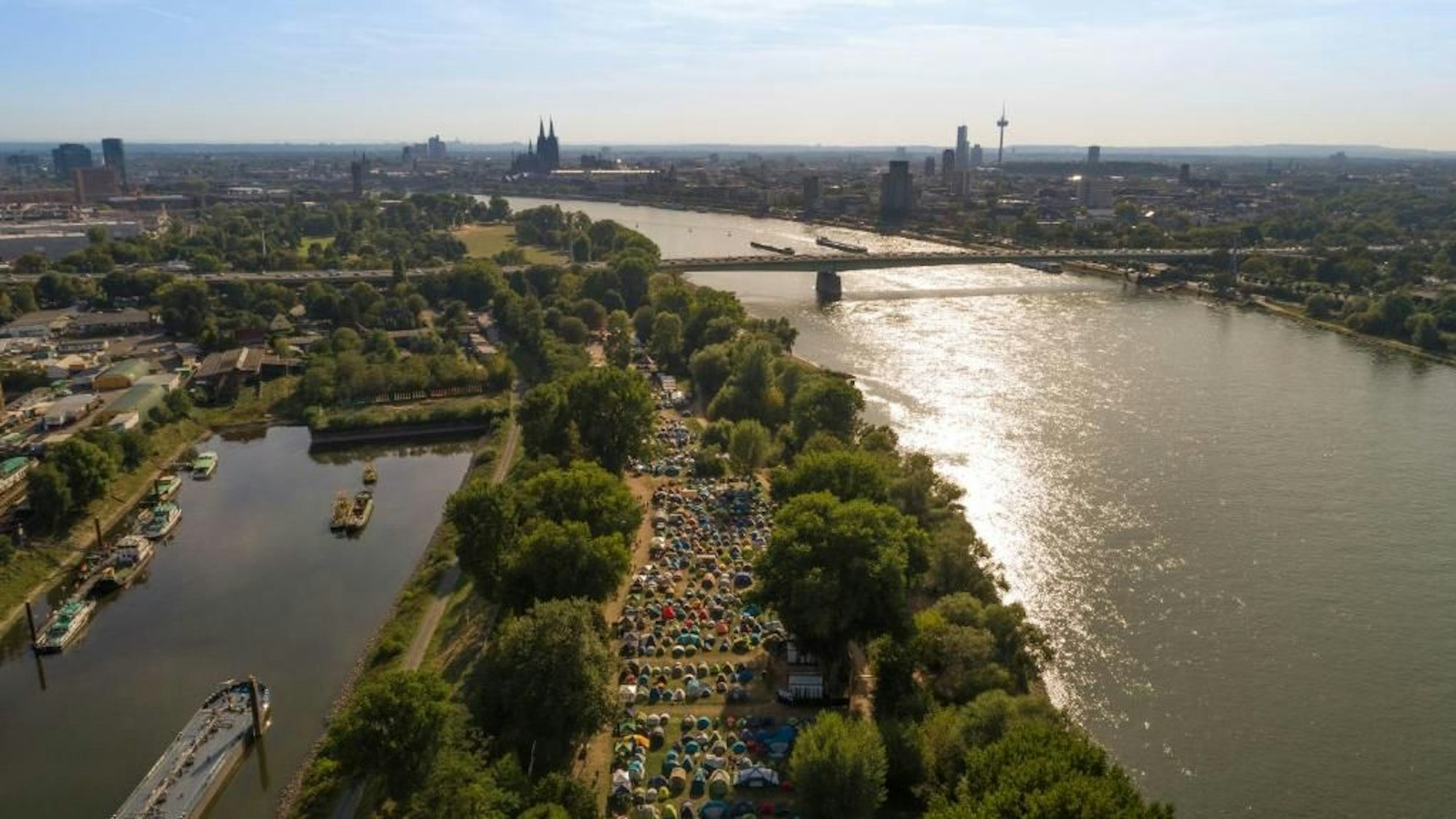 Schon während der Gamescom zelteten Besucher im Jugendpark: Ein Luftbild eines Zeltlagers auf der Landzunge am Rhein, im Hintergrund Kölns Skyline mit dem Dom.