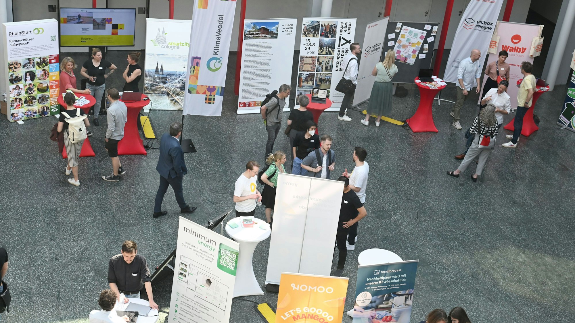 Das Foto zeigt Menschen, die eine Messe besuchen. Zu sehen sind auch Stehtische und Werbe-Aufsteller.