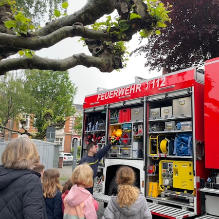 Ein Feuerwehrmann zeigt Kindern ein Feuerwehrfahrzeug.