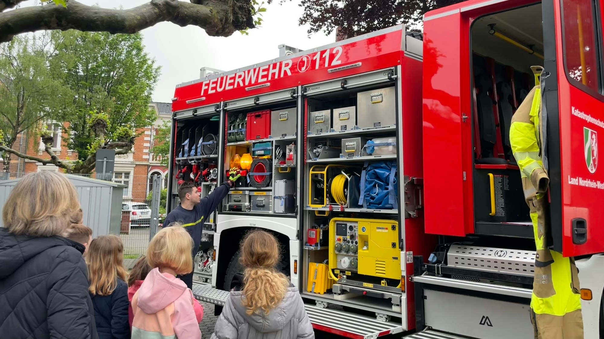Ein Feuerwehrmann zeigt Kindern ein Feuerwehrfahrzeug.