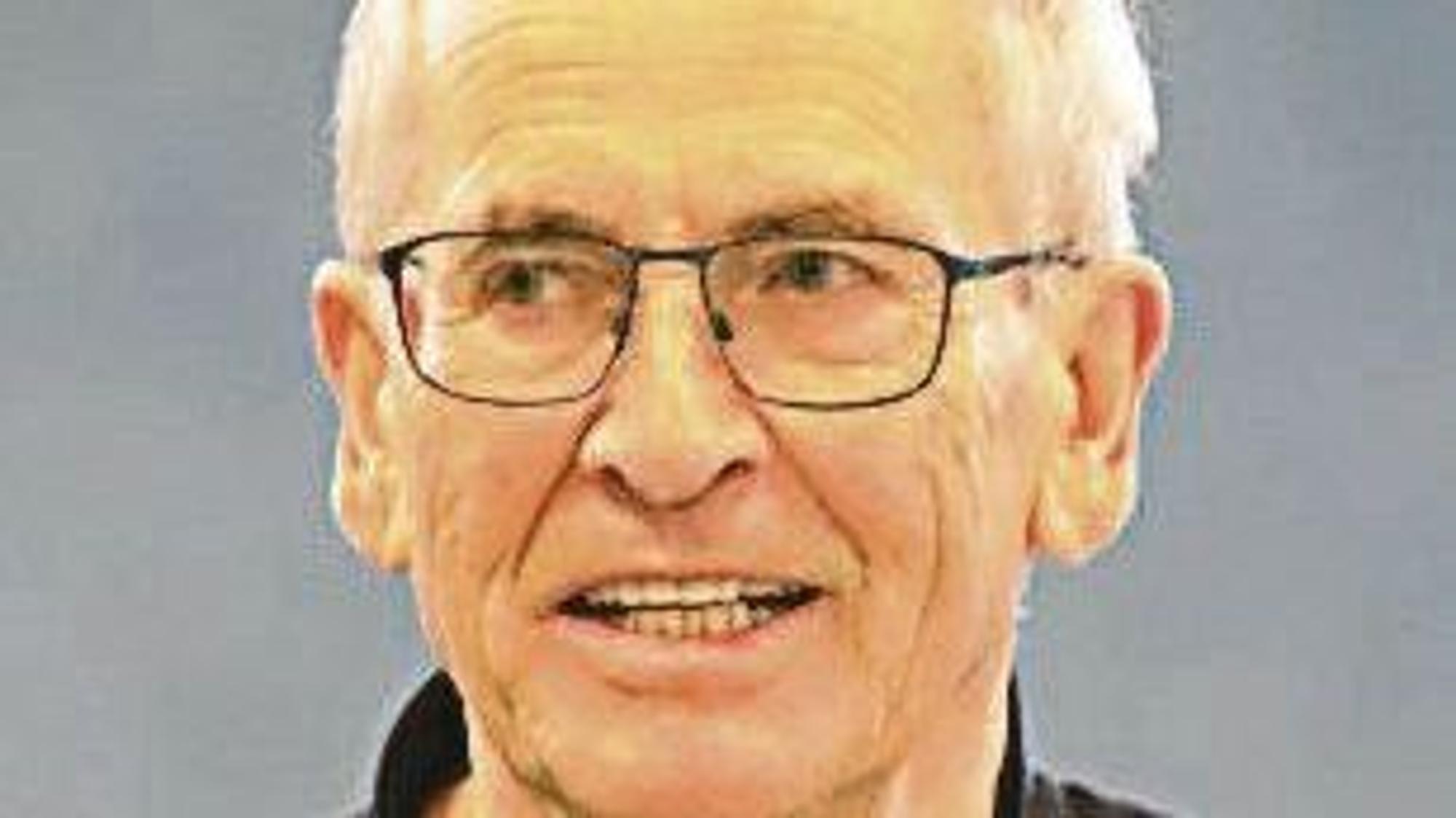 Ein Mann mit weißen Haaren und einer dünnrandigen schwarzen Brille.