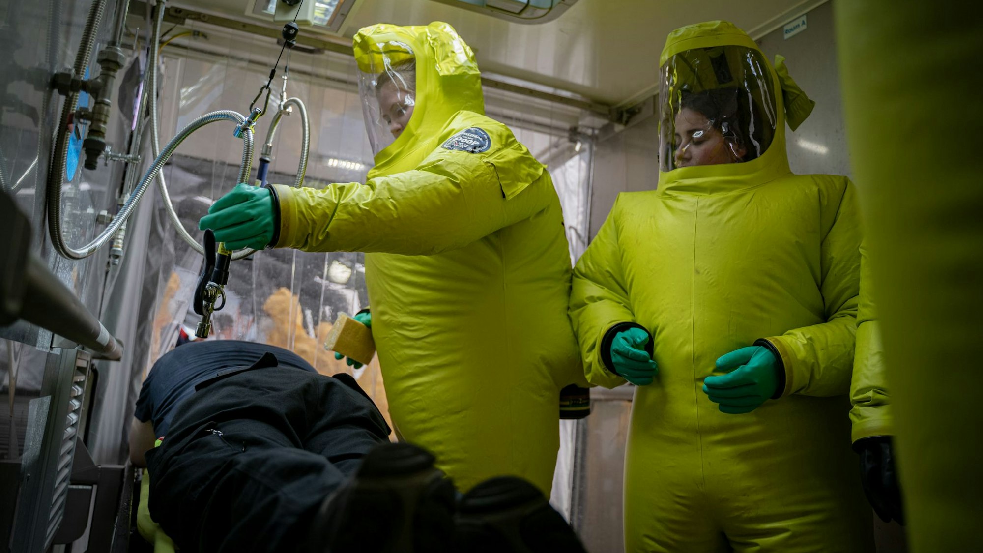 Auf dem Foto sind Feuerwehrleute in Schutzanzügen zu sehen, die einen Kollegen, der einen Patienten mimt, behandeln.