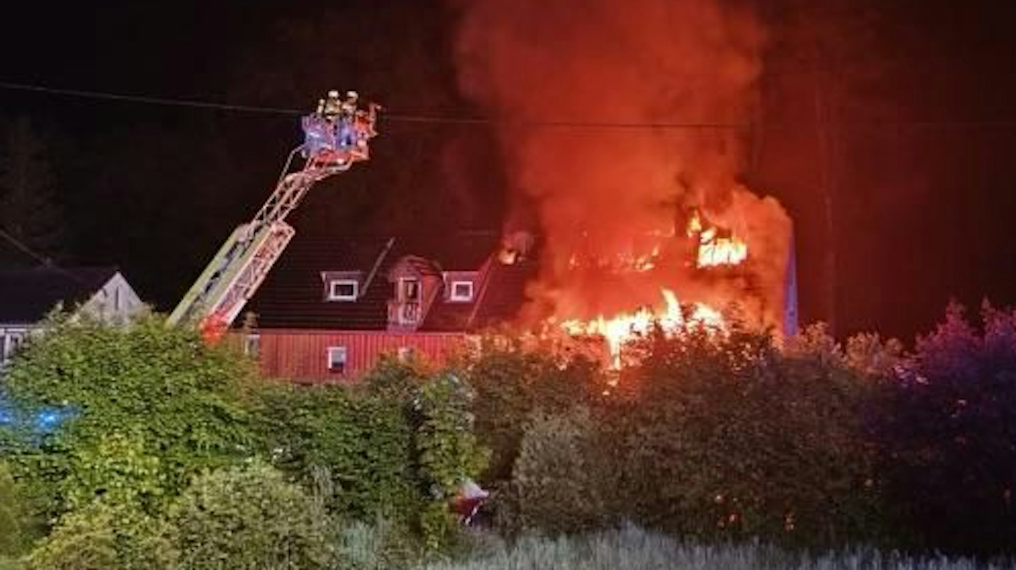 Ein Haus steht lichterloh in Flammen, die Feuerwehr löscht unter anderem mit Hilfe einer Drehleiter.