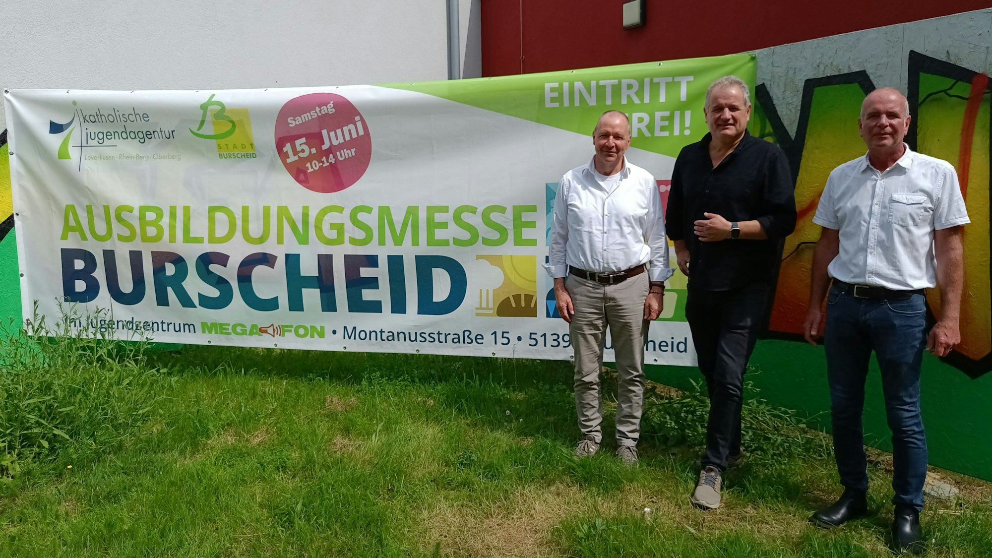 Drei Männer posieren vor einem Banner. Auf dem steht: „Ausbildungsmesse Burscheid, Eintritt frei“.