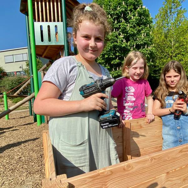 Zu sehen sind drei Kinder beim Bau eines hölzernen Hochbeets.
