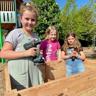 Zu sehen sind drei Kinder beim Bau eines hölzernen Hochbeets.