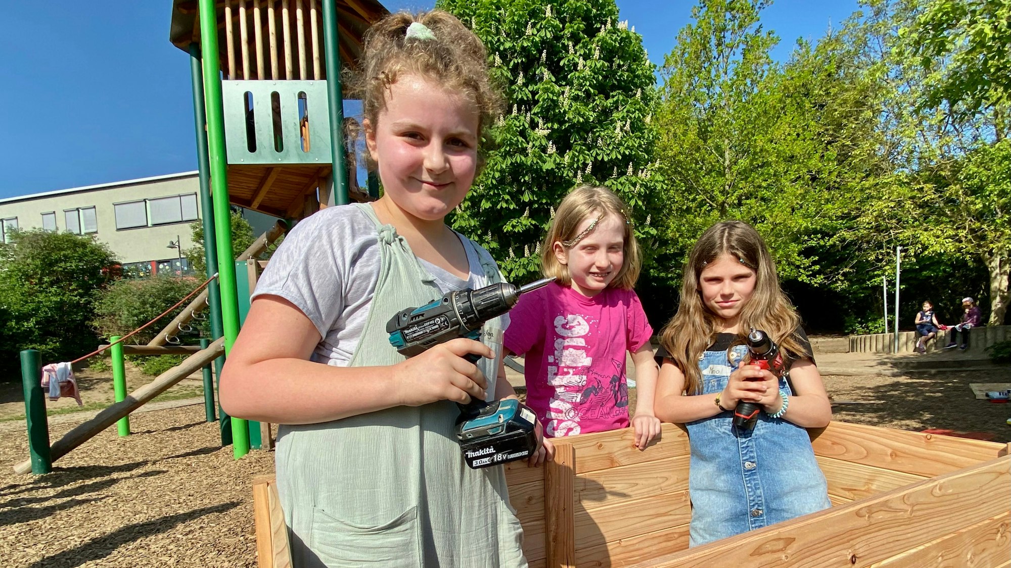 Zu sehen sind drei Kinder beim Bau eines hölzernen Hochbeets.