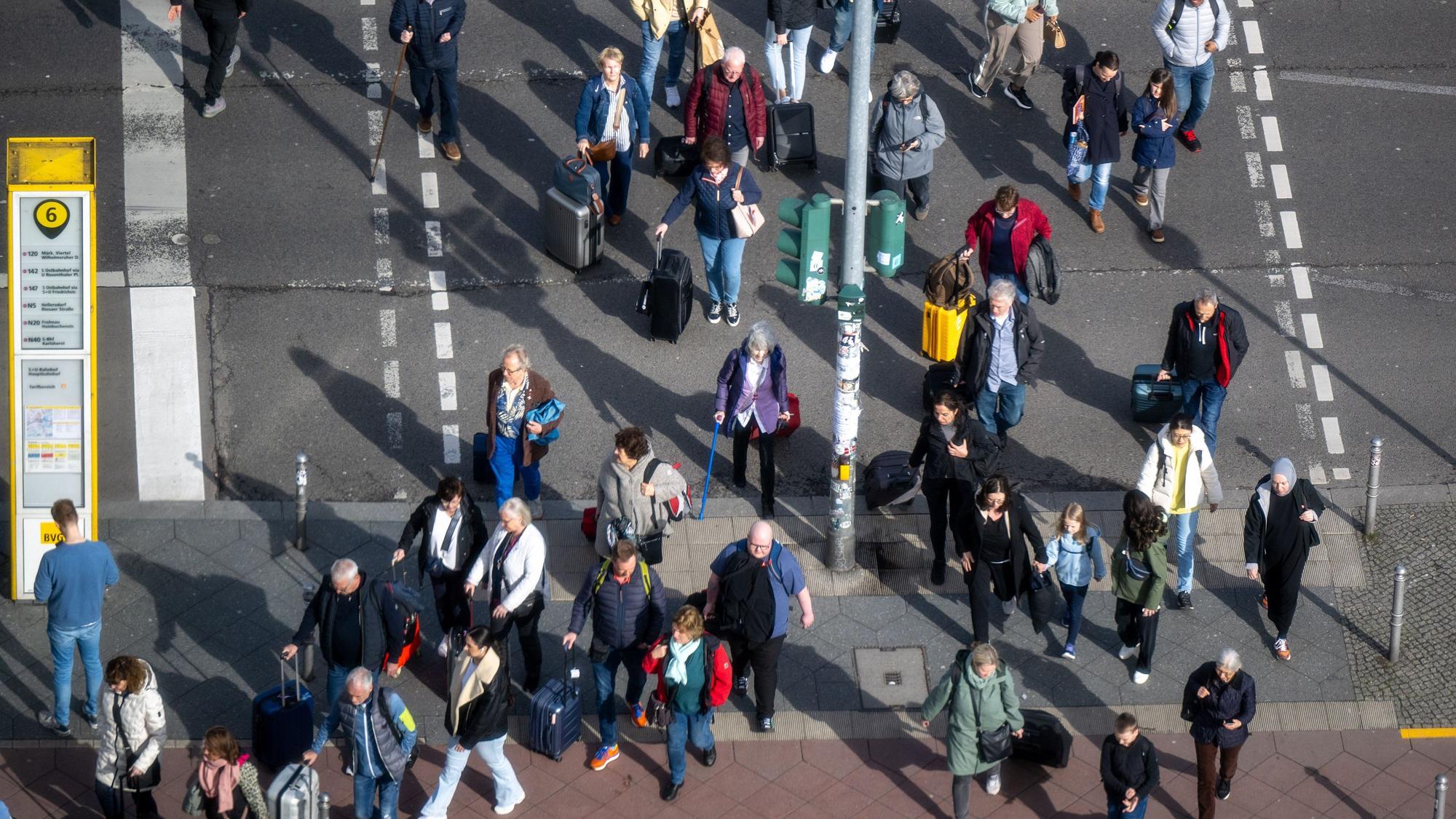 Zahlreiche Menschen mit Koffern und Rucksäcken überqueren eine Straße und gehen in Richtung Hauptbahnhof.