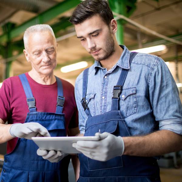 Team of engineers in overalls using digital tablet together while standing in production department of modern plant