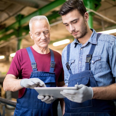 Team of engineers in overalls using digital tablet together while standing in production department of modern plant