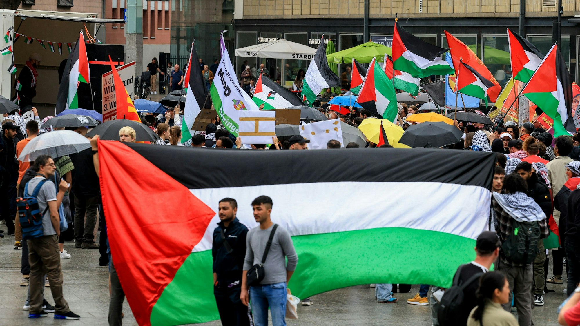 Menschen mit Palästina-Flaggen stehen auf dem Bahnhofsvorplatz in Köln.