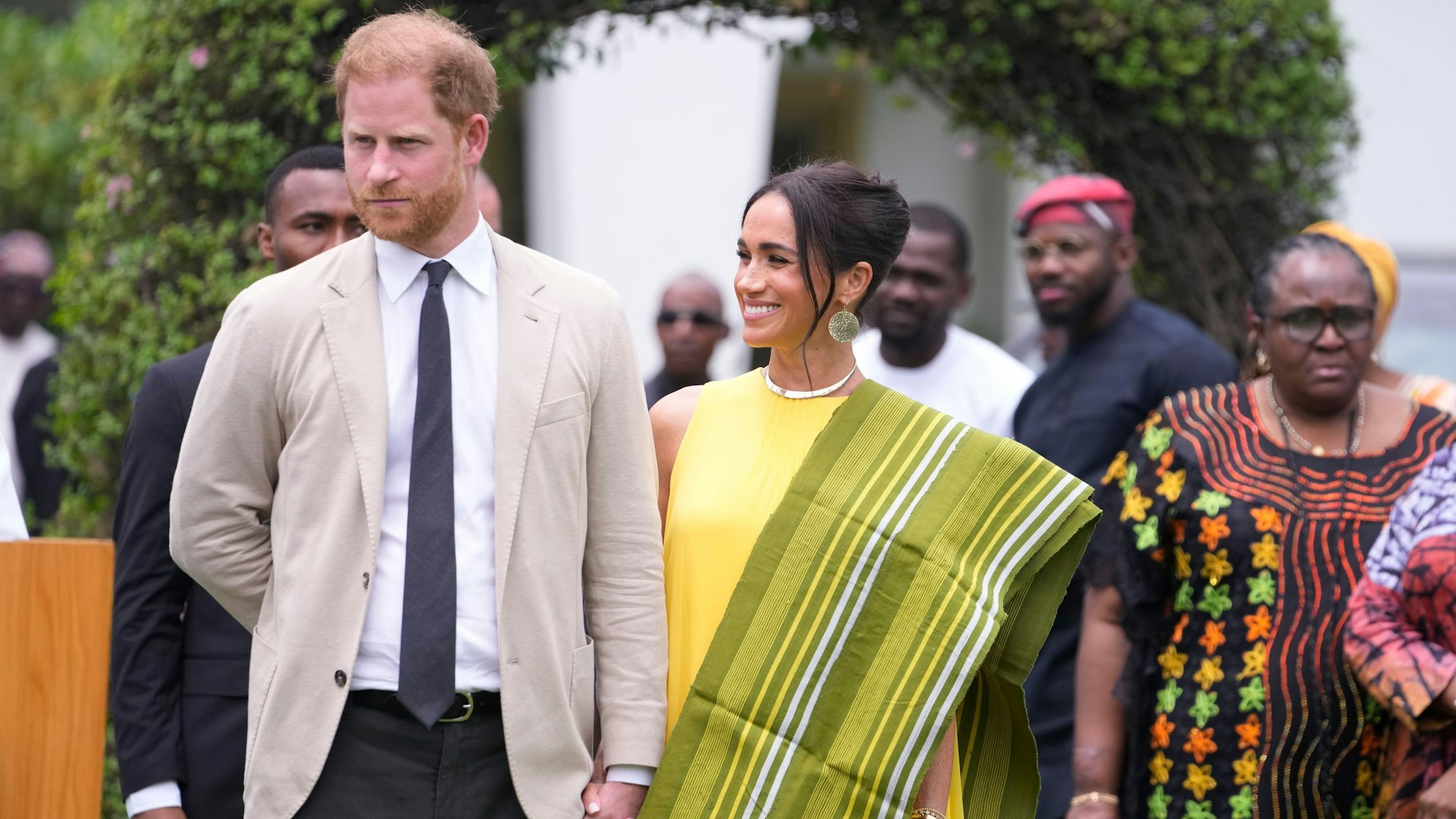 Prinz Harry und seine Frau Meghan halten Hand und lächeln.