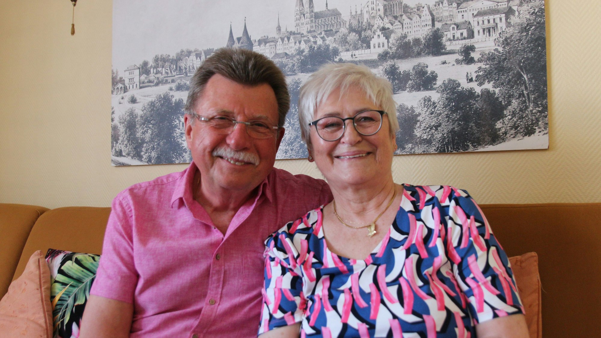 Die Eheleute sitzen auf einem Sofa und lächeln in die Kamera.