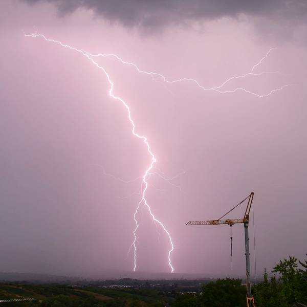Ein gewaltiger Blitz schlägt am vom Unwetter lila gefärbten Himmel in der Nähe eines Baukrans ein. Schwere Unwetter werden in der Nacht zu Freitag in Köln und der Region erwartet. (Archivbild)