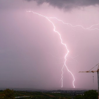 Ein gewaltiger Blitz schlägt am vom Unwetter lila gefärbten Himmel in der Nähe eines Baukrans ein. Schwere Unwetter werden in der Nacht zu Freitag in Köln und der Region erwartet. (Archivbild)