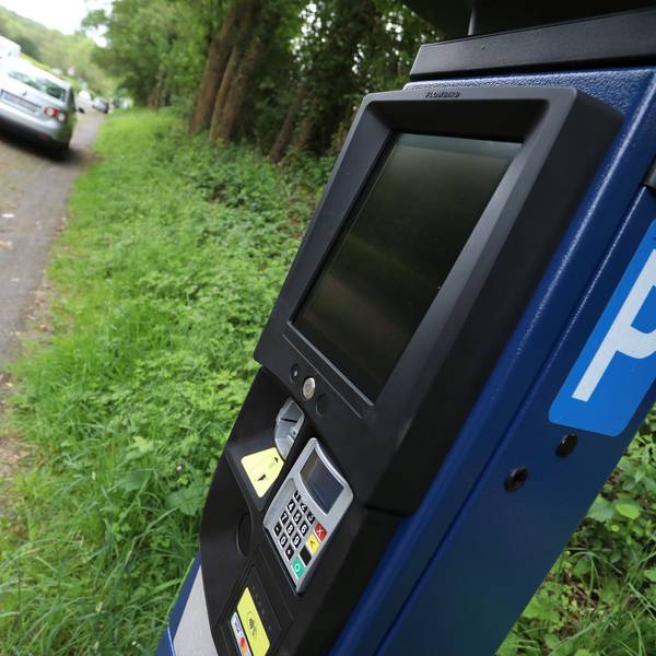 Ein Parkscheinautomat und ein parkendes Auto im Hintergrund.