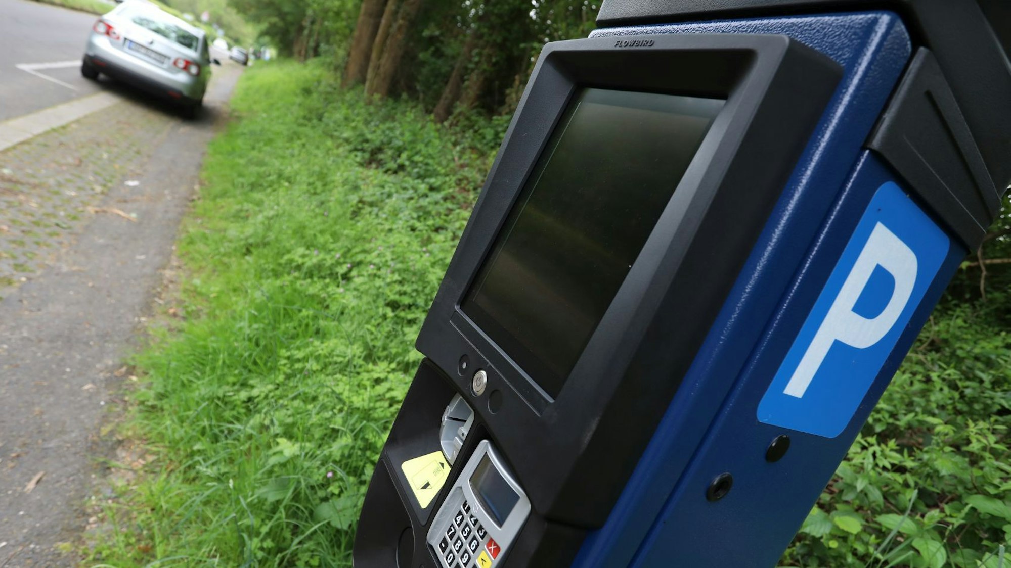 Ein Parkscheinautomat und ein parkendes Auto im Hintergrund.