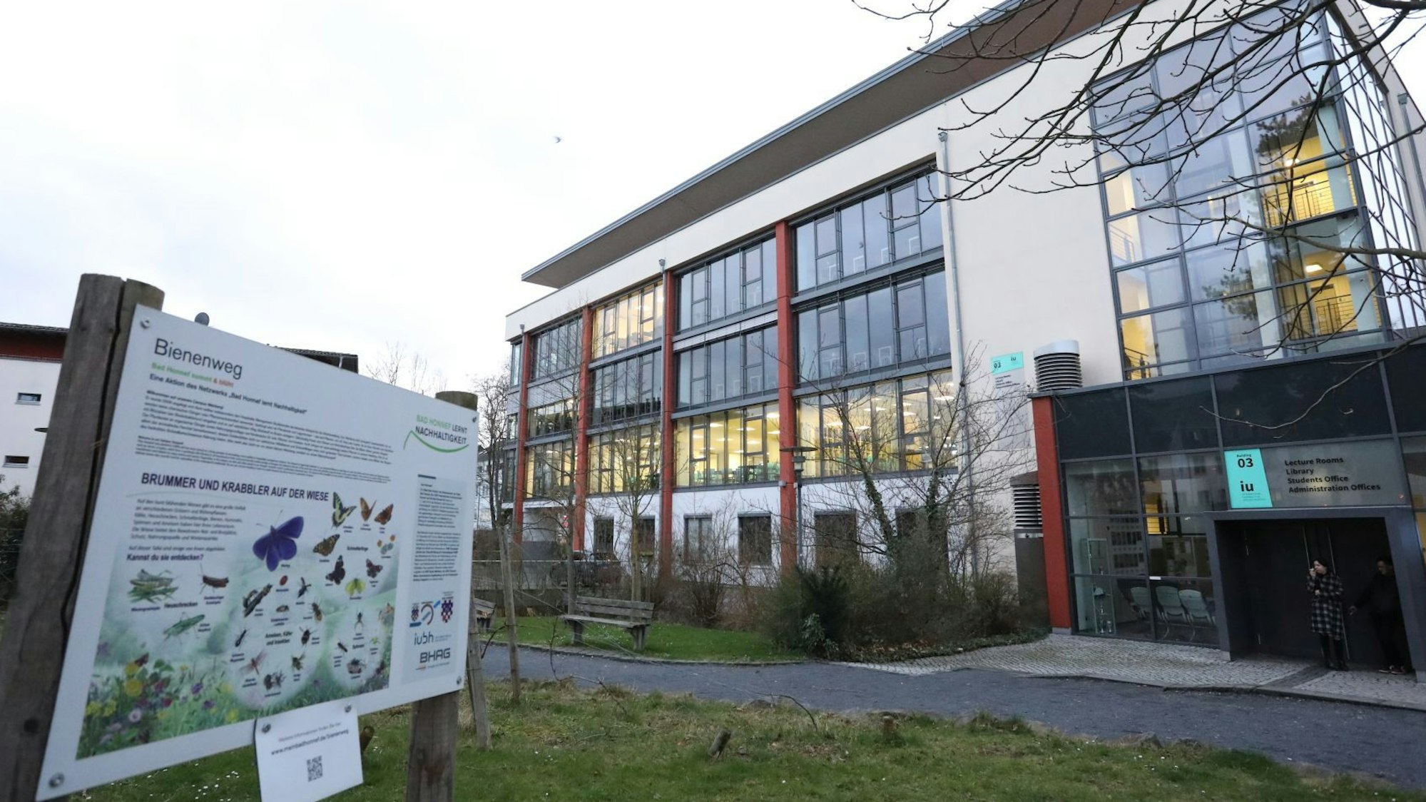 Ein Gebäude mit einer Bank davor, aus einigen Fenstern scheint Licht.