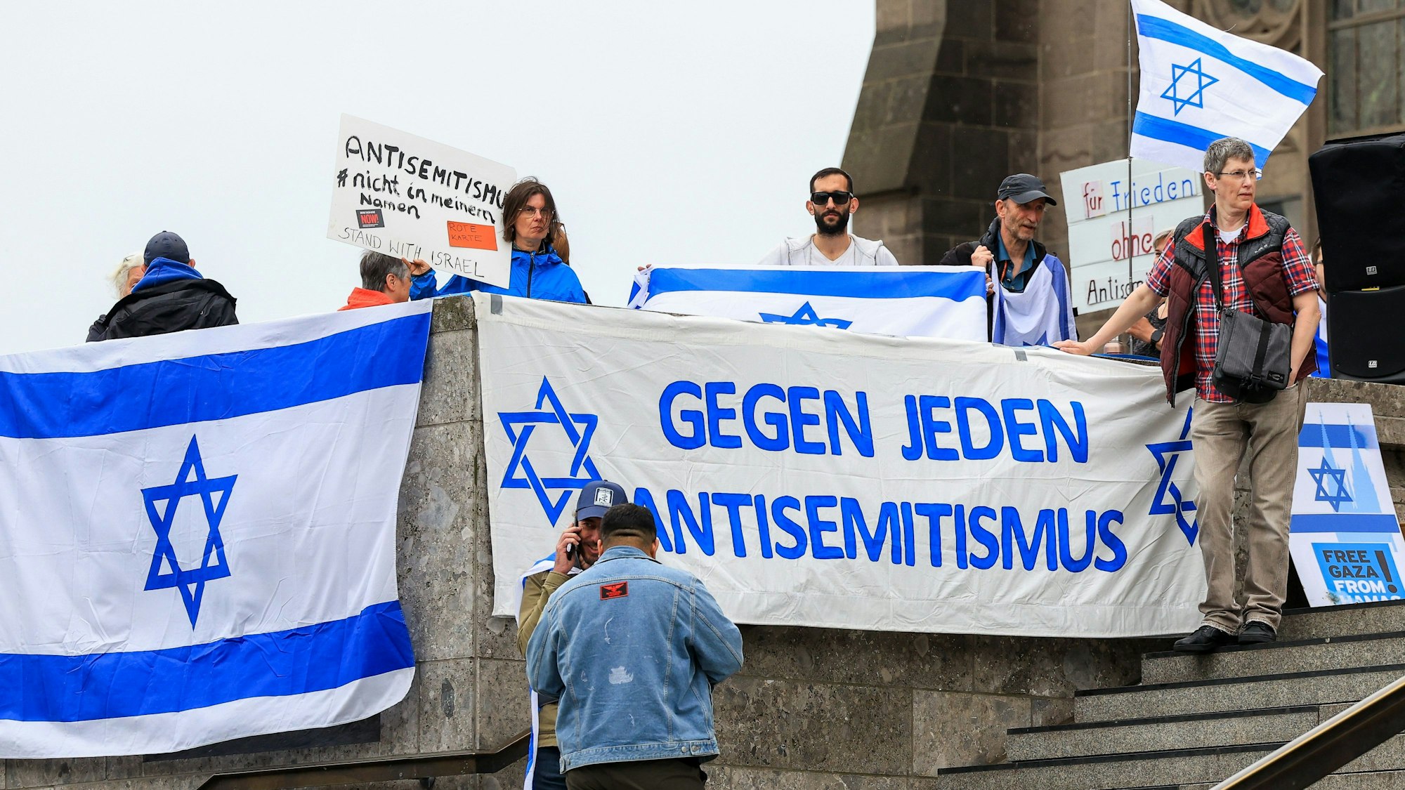Menschen mit Israel-Flaggen am Kölner Dom, auf einem Transparent ist „Gegen jeden Antisemitismus“ zu lesen.