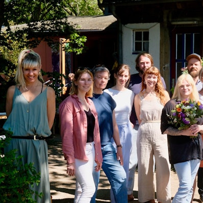 Anna Theusch mit einem Blumenstrauss von Gratulantin Cornelia Weitekamp (3.v.r.) ihrem Team und Mitgliedern vom Vereinsvorstand des Universitätskindergarten.