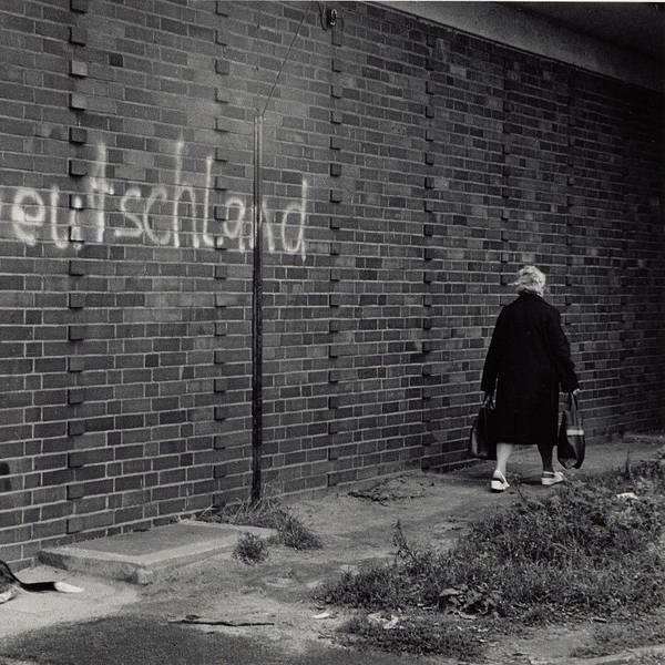 Eine Frau geht an einer Mauer vorbei, auf der das gesprühte Wort Deutschland steht.