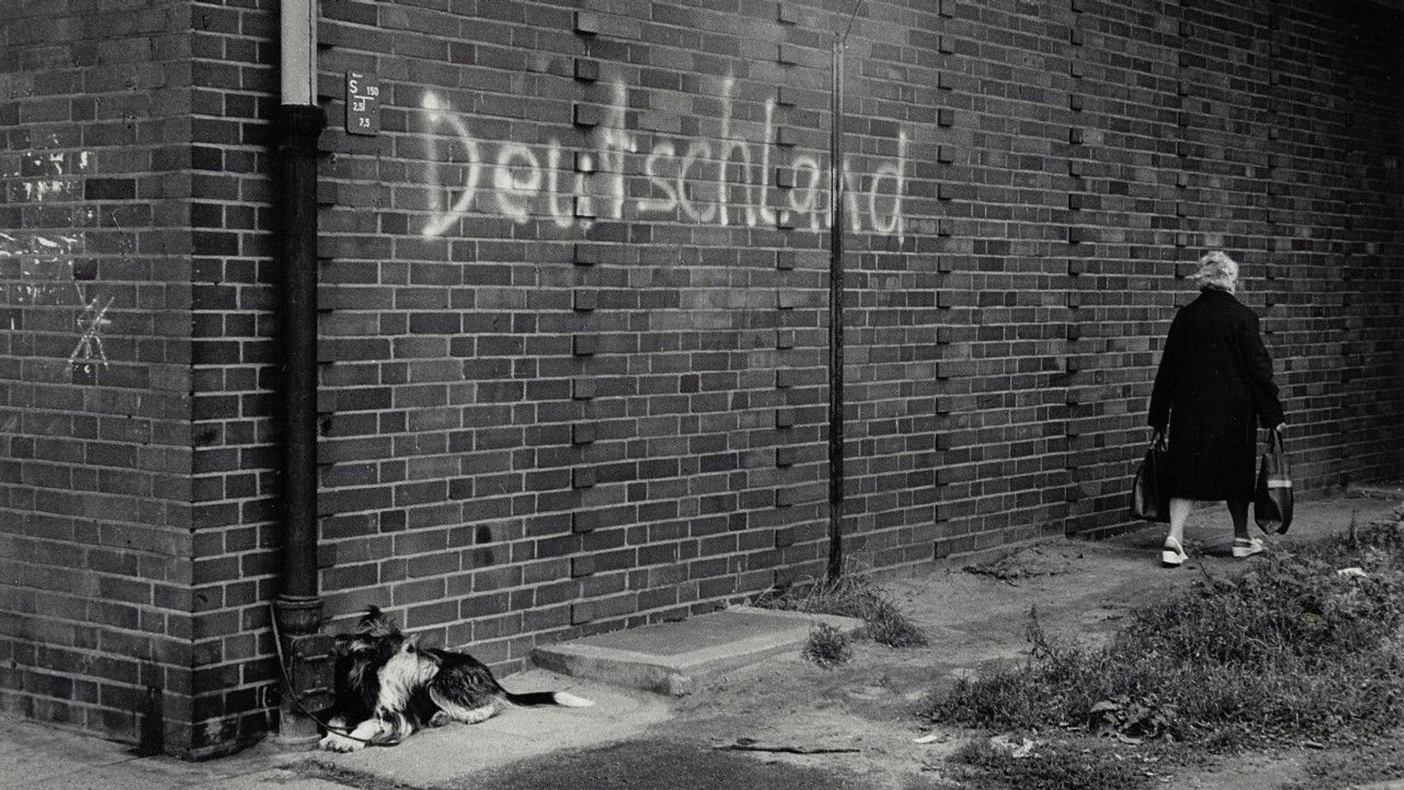 Eine Frau geht an einer Mauer vorbei, auf der das gesprühte Wort Deutschland steht.