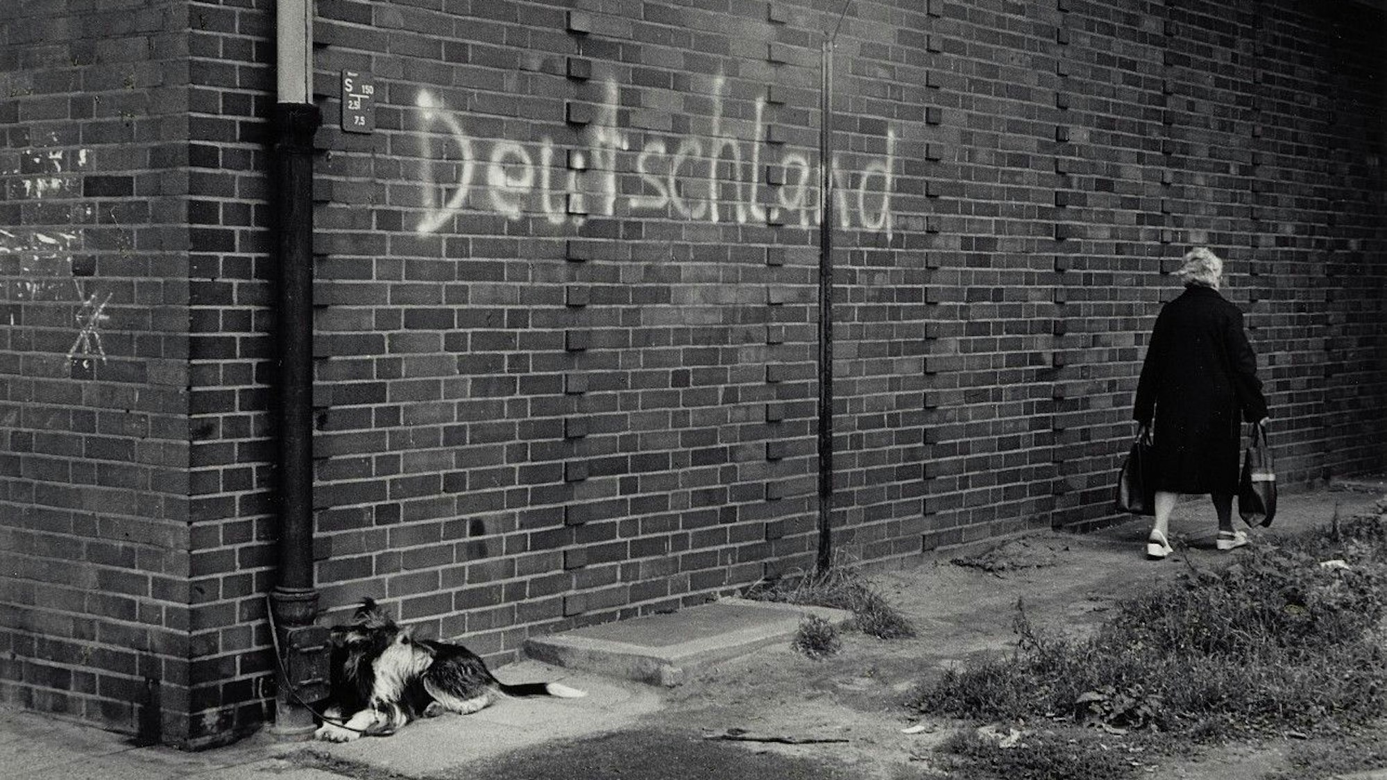 Eine Frau geht an einer Mauer vorbei, auf der das gesprühte Wort Deutschland steht.