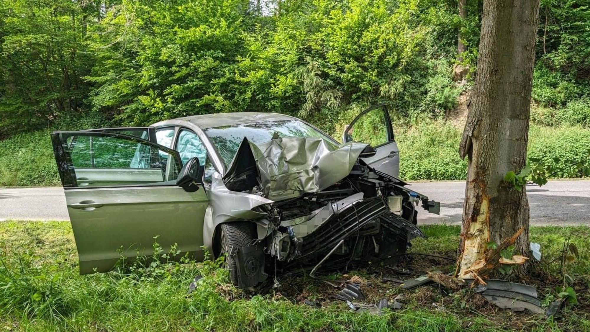Ein zerstörtes Auto steht neben einem Baum.