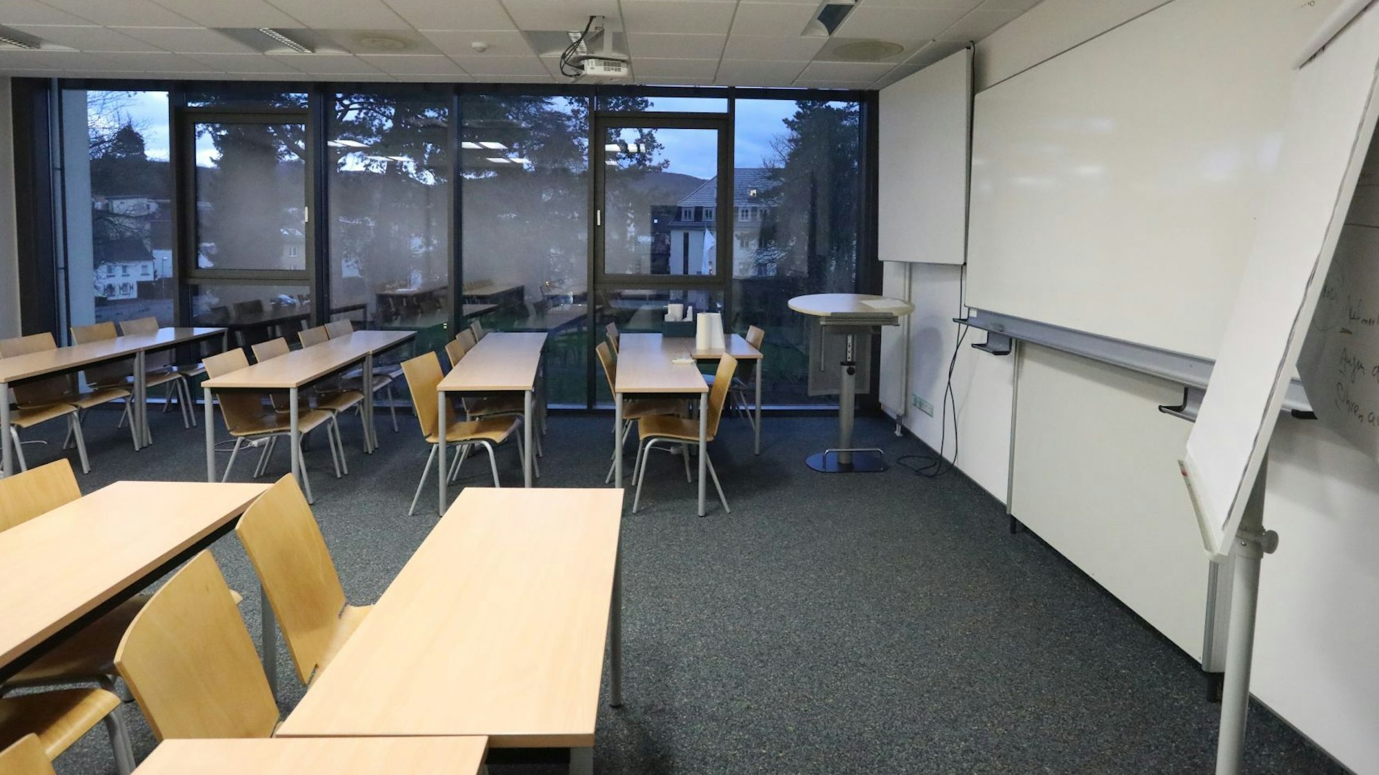 Ein Raum mit beigen Stühlen und Tischen und einem Whiteboard an der Wand.