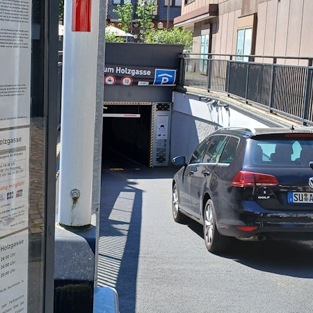 Ein Auto fährt in eine Tiefgarage; links stehen auf einer Tafel die Tarife.