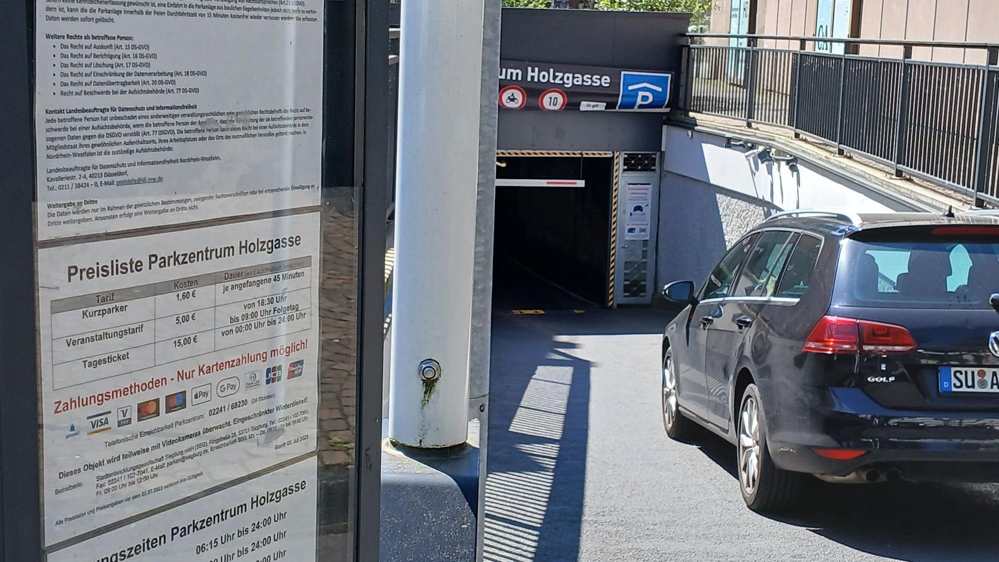 Ein Auto fährt in eine Tiefgarage; links stehen auf einer Tafel die Tarife.