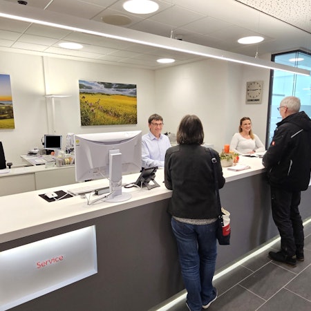 Die Servicemitarbeiter Egon Ronig und Denise Maletzki stehen am Schalter und bedienen zwei Kunden.