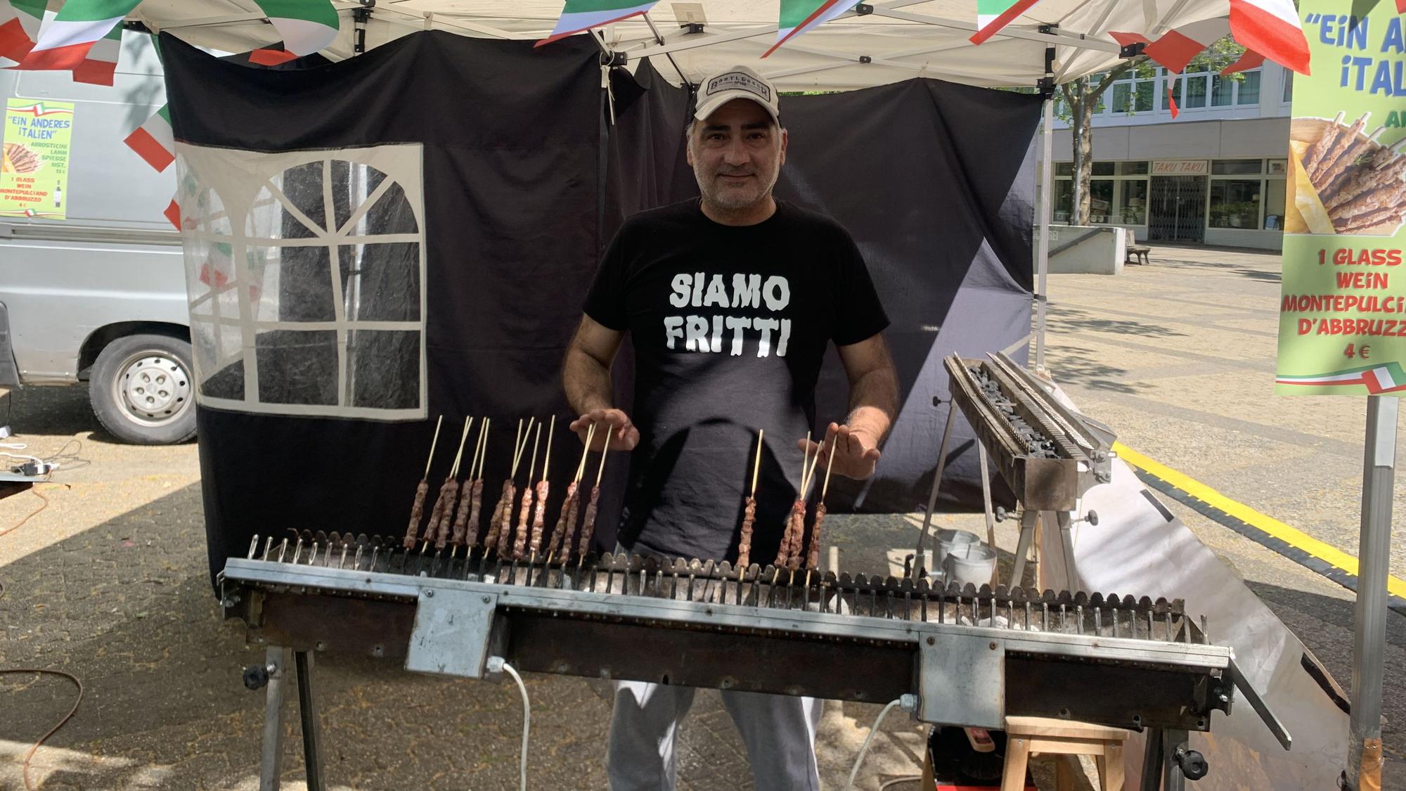 Auf dem Foto ist ein Mann zu sehen, der auf einem Grill Fleischspieße zubereitet.